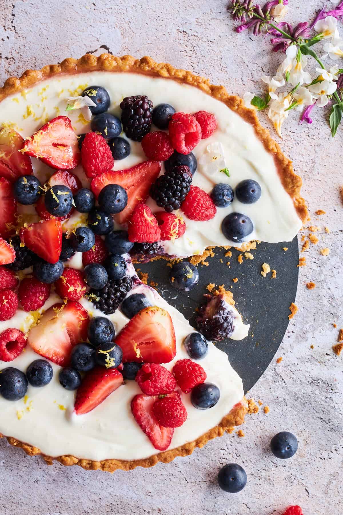 Draufsicht auf eine Käsekuchen-Obst-Tarte, von der ein Stück fehlt. 