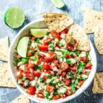 Overhead shot of homemade pico de gallo with lime wedges and tortilla chips.