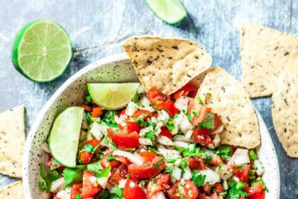 Overhead shot of homemade pico de gallo with lime wedges and tortilla chips.