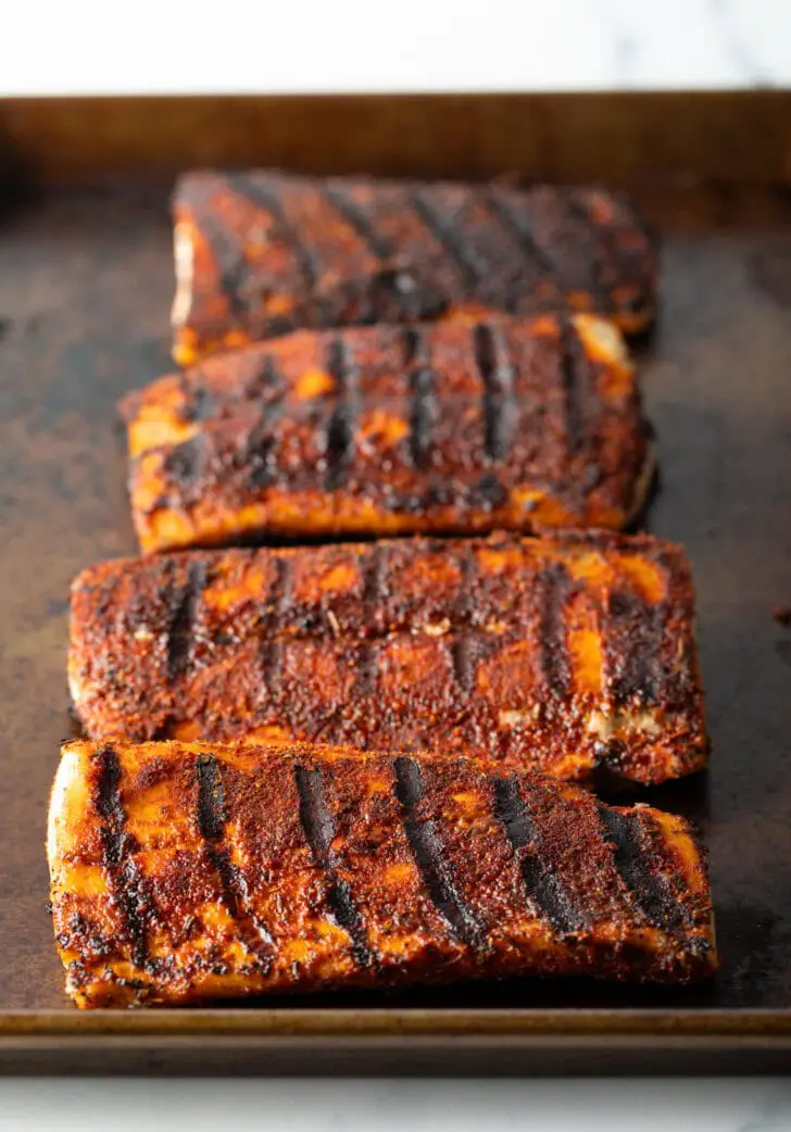 4 große gegrillte Fischfilets auf einem mit Blackening-Gewürz bestrichenen Backblech.