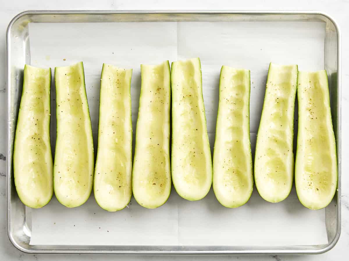 Zucchini aushöhlen, halbieren und auf einem mit Backpapier ausgelegten Backblech würzen. 