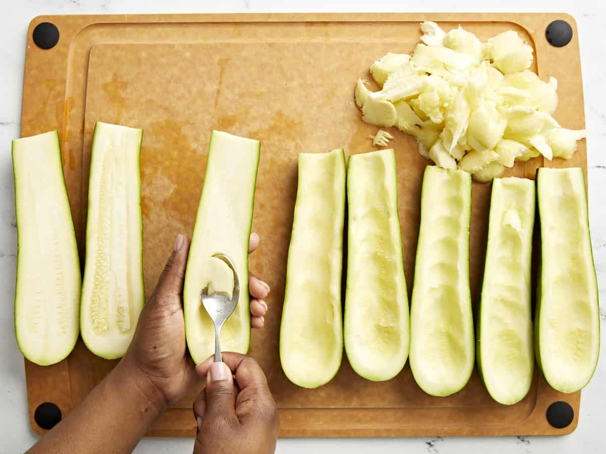 Das Fruchtfleisch wird auf einem Schneidebrett aus der Zucchini herausgelöffelt.