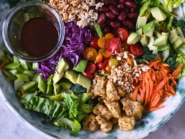 Salz- und Pfeffertofu in einer großen Schüssel mit Salatzutaten wie Ramennudeln, zerkleinertem Salat und Karotten