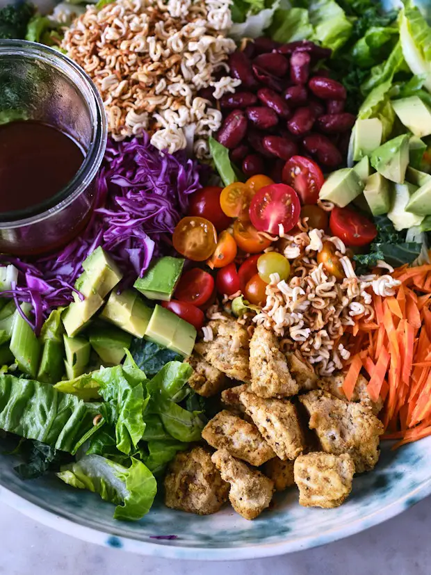 Salz- und Pfeffertofu in einer großen Schüssel mit Salatzutaten wie Ramennudeln, zerkleinertem Salat und Karotten