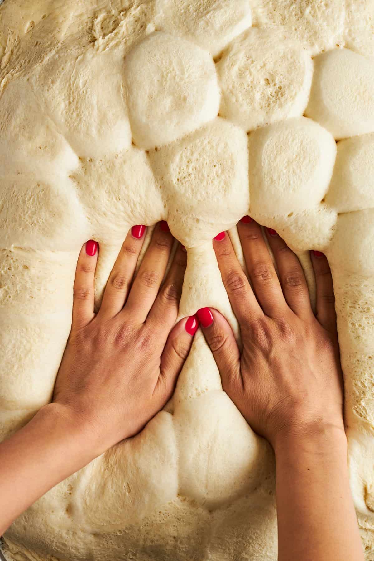 Zwei Hände drücken rohe Brötchen nach unten, um eine flache Kruste zu formen. 