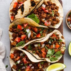 Fünf Tacos auf einem Schneidebrett, daneben Limetten