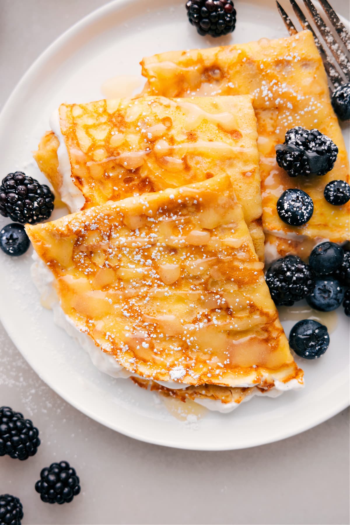 Teller mit drei Crêpes, darüber geträufelt mit Beeren und Sirup.