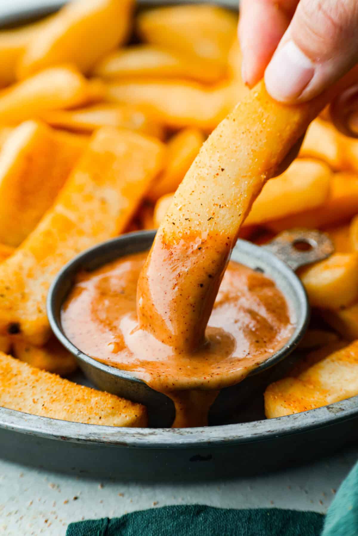 Nahaufnahme von jemandem, der Pommes in eine kleine Schüssel mit Re-Robin-Lagerfeuersauce taucht. 