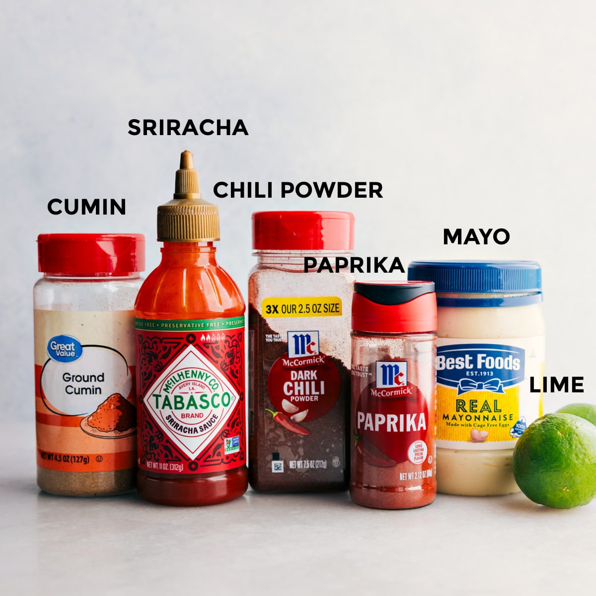 Alle Dressing-Zutaten, einschließlich Kreuzkümmel, Sriracha, Chilipulver, Paprika, Mayonnaise und Limetten, sind für die einfache Zubereitung vorbereitet.