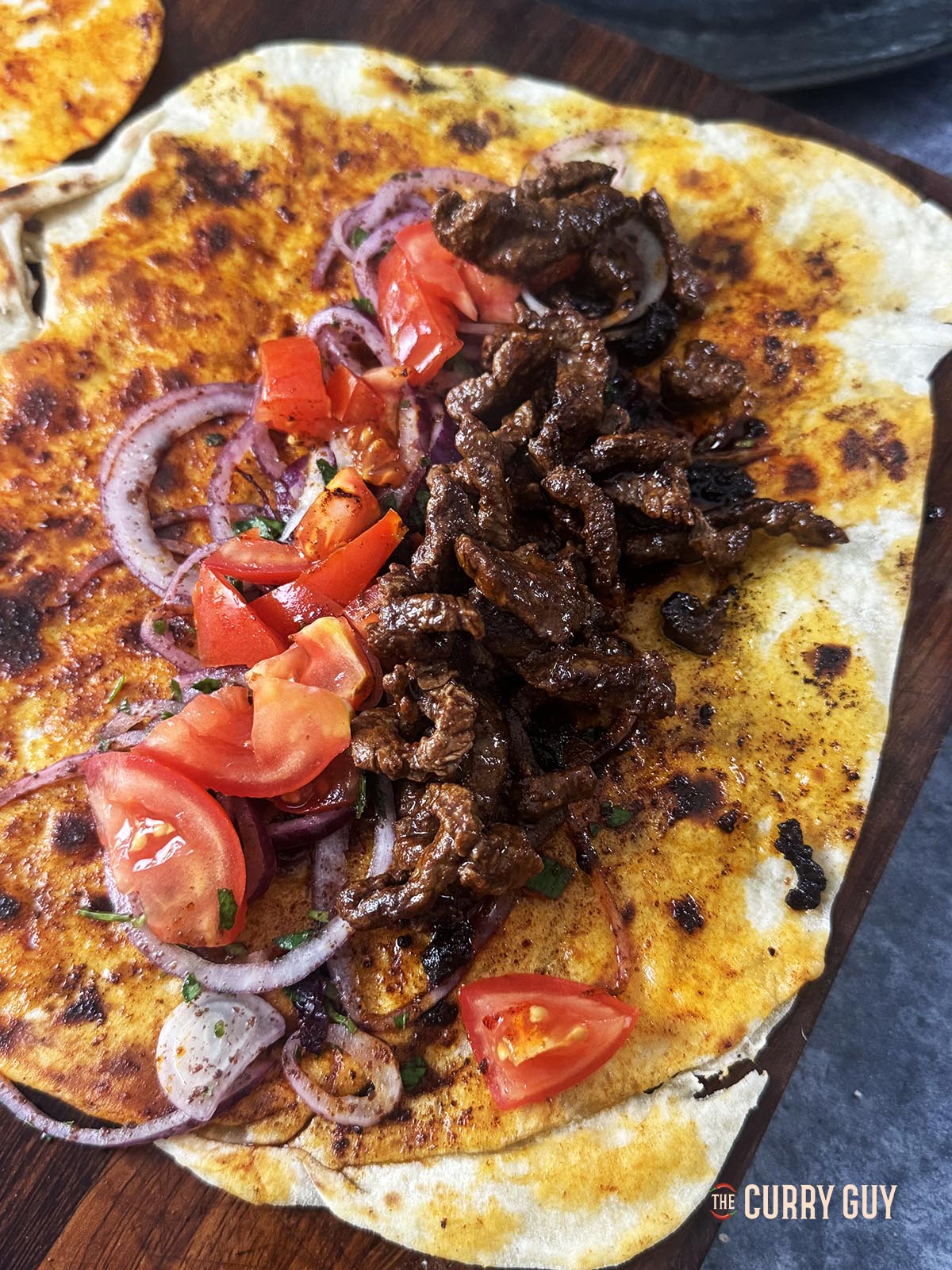 Belegt wird ein Lavsh-Brot mit Zwiebelsalat, Tomatenwürfeln und gebratenem Rindfleisch.