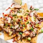 Luftaufnahme von frisch zubereiteten BBQ-Chicken-Nachos mit Limettenspalten an der Seite.