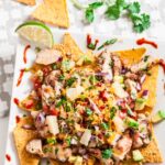 A plate of BBQ chicken nachos topped with diced vegetables, pineapple chunks, cheese, and fresh cilantro.