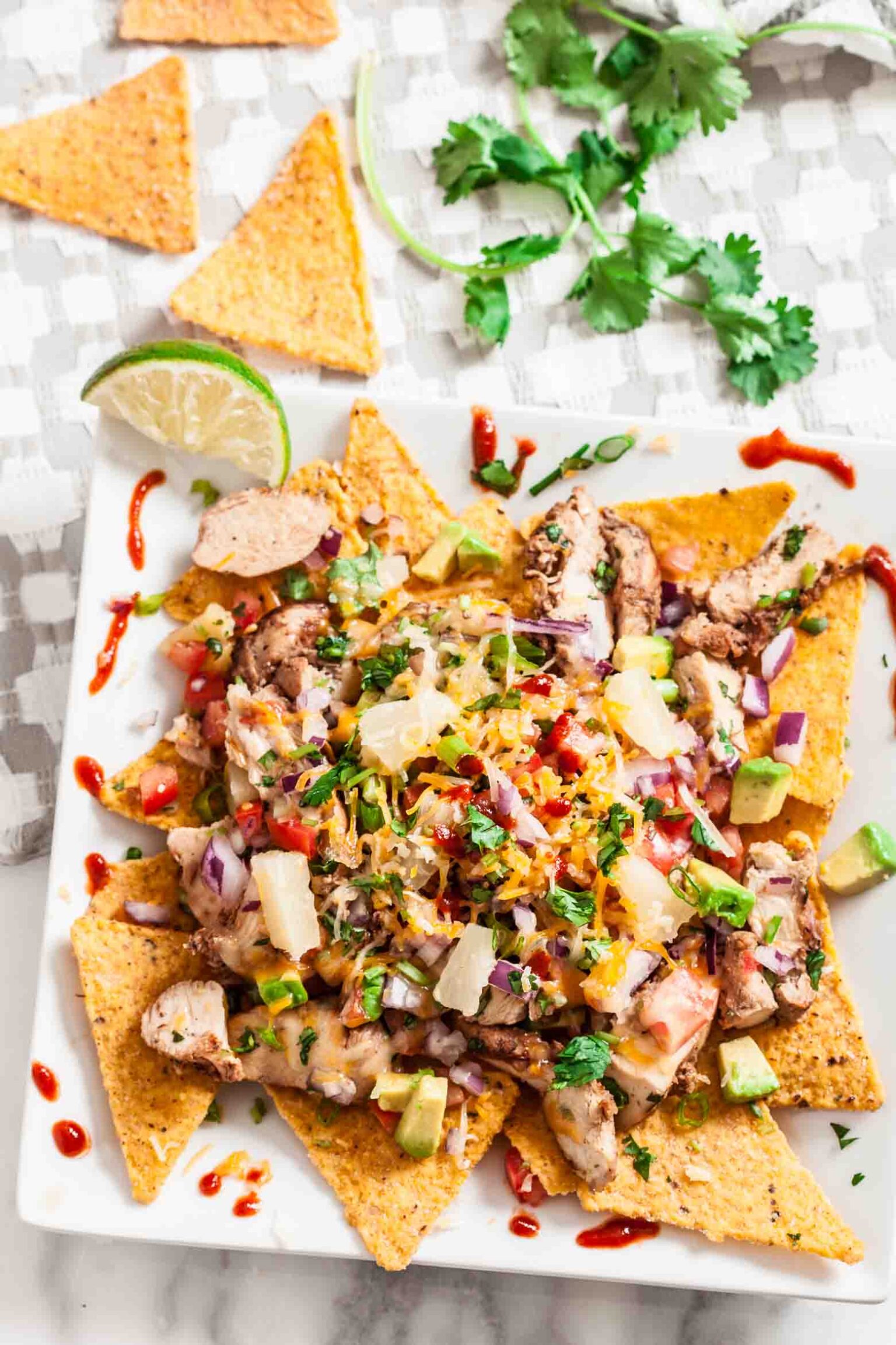 A plate of BBQ chicken nachos topped with diced vegetables, pineapple chunks, cheese, and fresh cilantro.