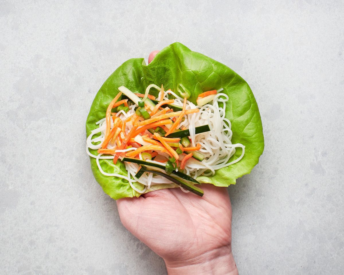 Salat, Nudeln und Gemüse in der Hand.