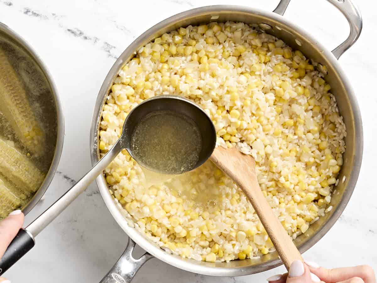 Eine Schöpfkelle gibt Gemüsebrühe zu Maisrisotto in einer Bratpfanne.