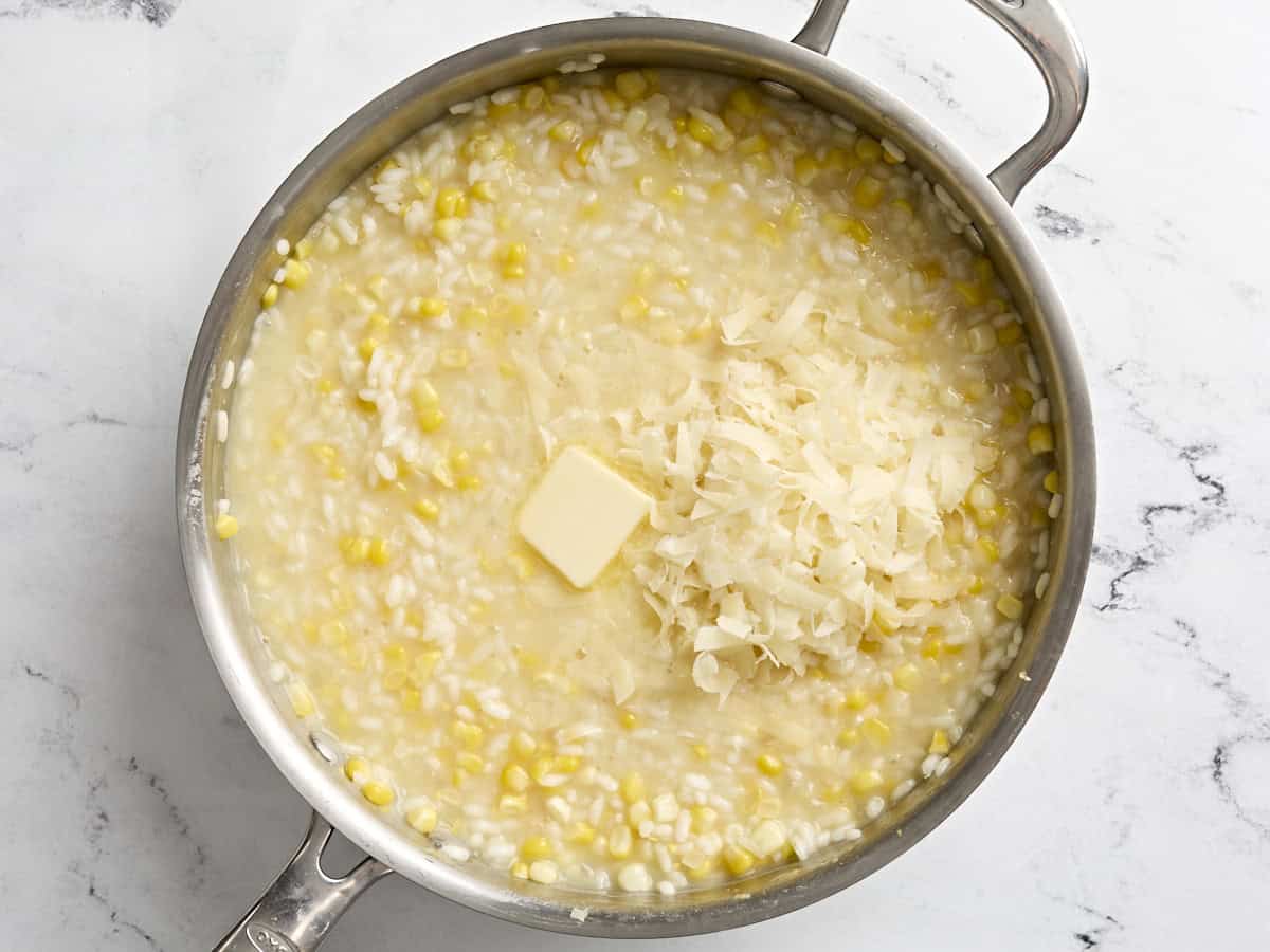 Ein Würfel Butter und geriebener Parmesankäse werden in einer Pfanne zu Maisrisotto gegeben.