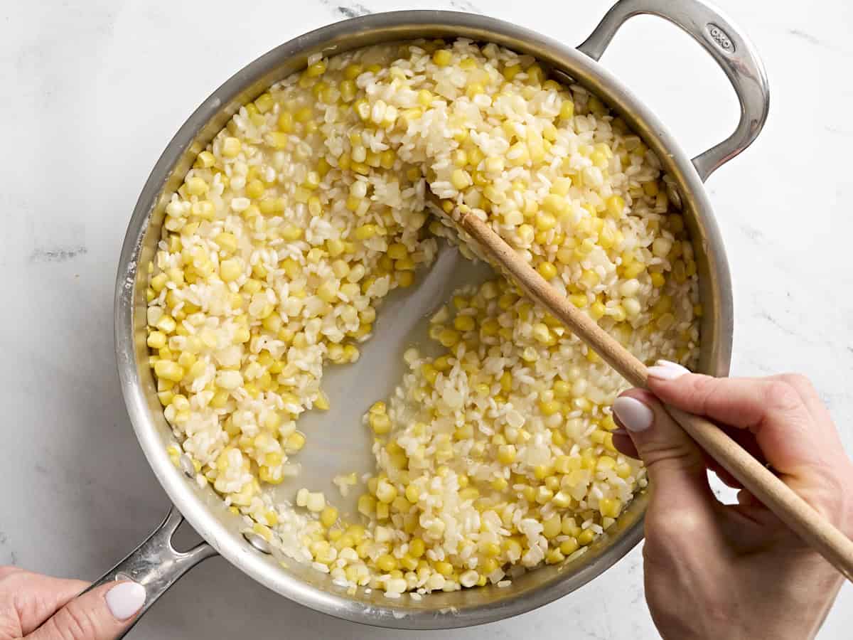 Ein Holzlöffel rührt Maisrisotto in einer Bratpfanne um.