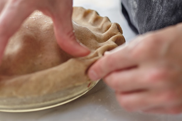 Die Ränder einer Beerenkuchenkruste mit Daumen und Fingern zusammendrücken