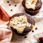 a chocolate cream cheese muffin is on a grey surface next to another cupcake