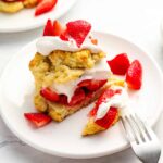 cut strawberry shortcake on a white plate with a fork.