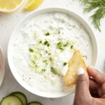 Overhead view of tzatziki sauce with a pita chip being dipped in the sauce.