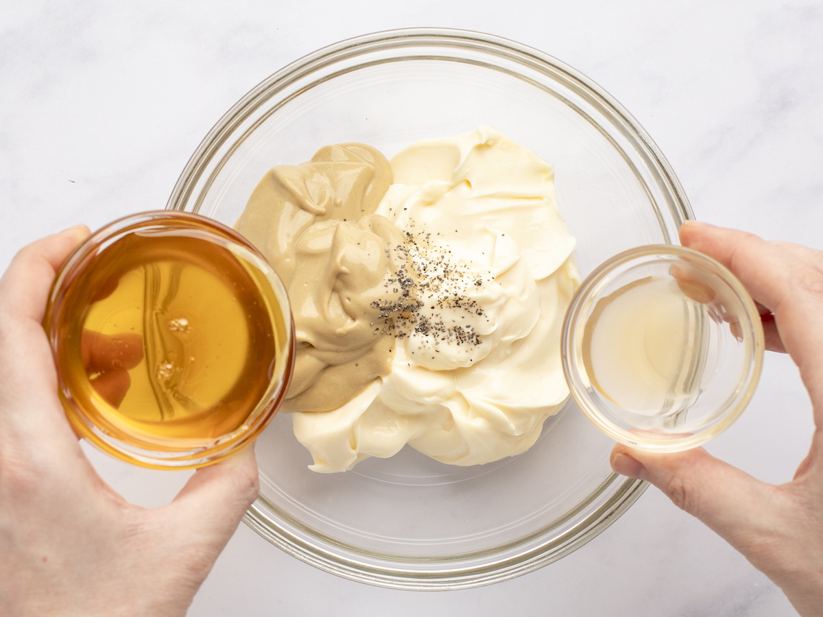 Gießen Sie Essig und Honig in eine Glasschüssel mit Senf, Mayonnaise und schwarzem Pfeffer