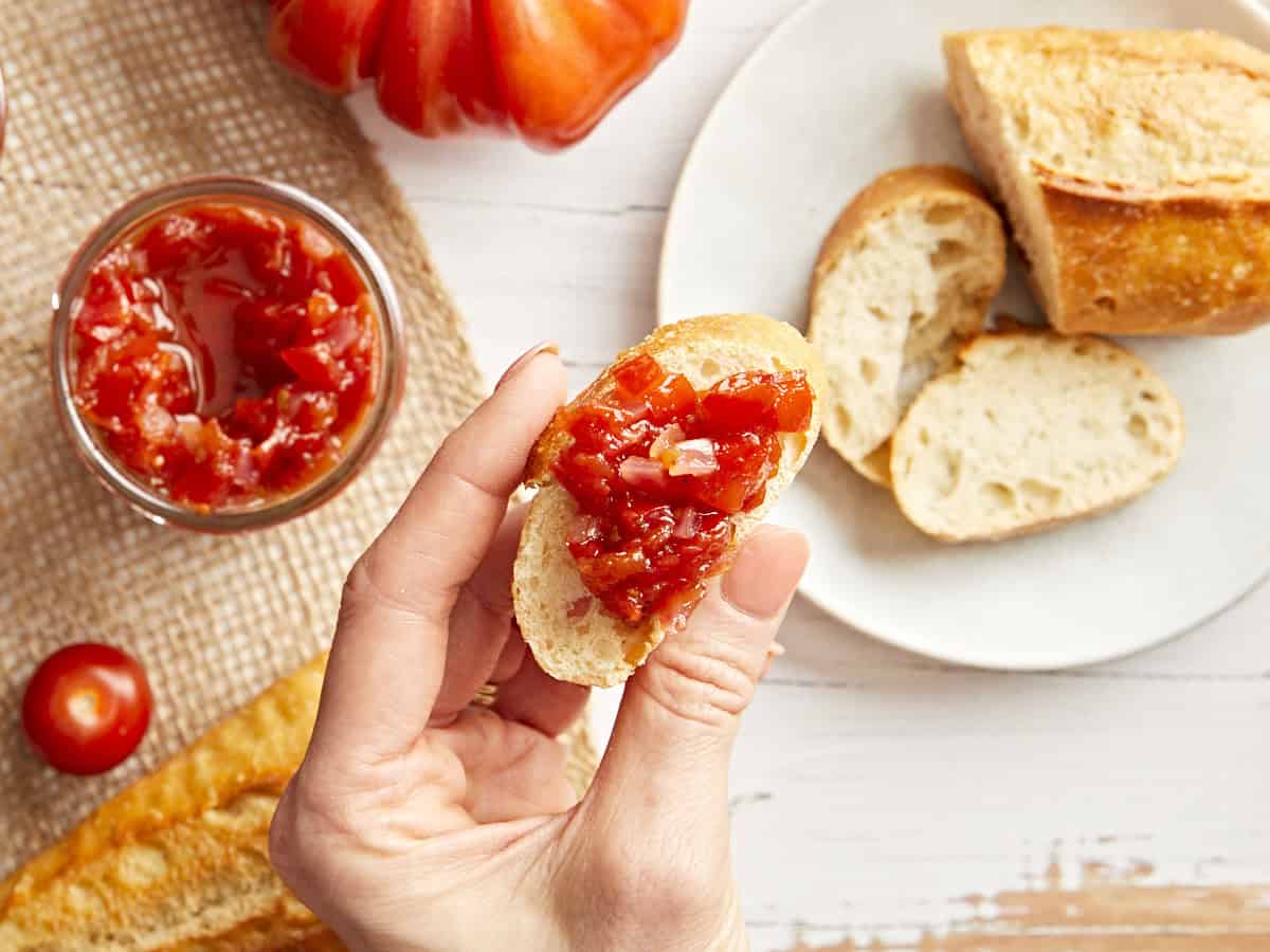 Eine Hand hält eine mit Tomatenrelish belegte Scheibe Brot.