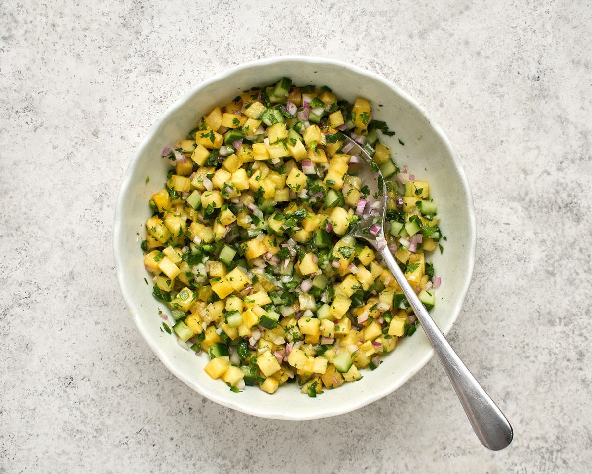 Ananas, Limettensaft, Zwiebel, Gurke, Jalapeño-Pfeffer, Zucker, Pflanzenöl, Salz und Koriander in einer weißen Schüssel kombiniert