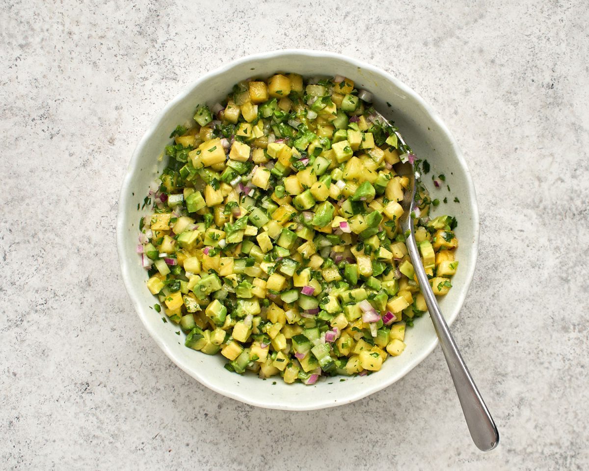 Avocado gemischt mit Ananas, Limettensaft, Zwiebel, Gurke, Jalapeño-Pfeffer, Zucker, Pflanzenöl, Salz und Koriander in einer weißen Schüssel