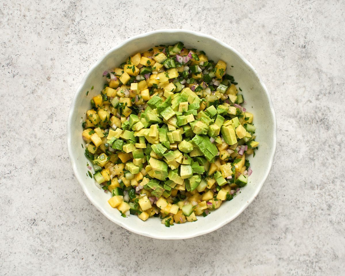 gewürfelte Avocado auf kombinierter Ananas, Limettensaft, Zwiebel, Gurke, Jalapeño-Pfeffer, Zucker, Pflanzenöl, Salz und Koriander in einer weißen Schüssel