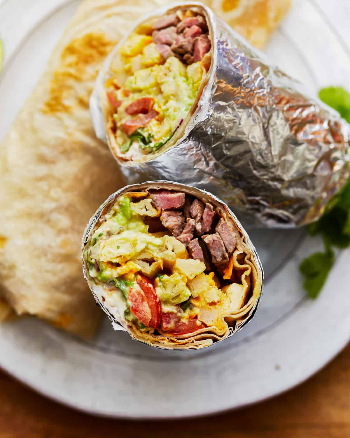 A halved california burrito wrapped in foil on a plate.