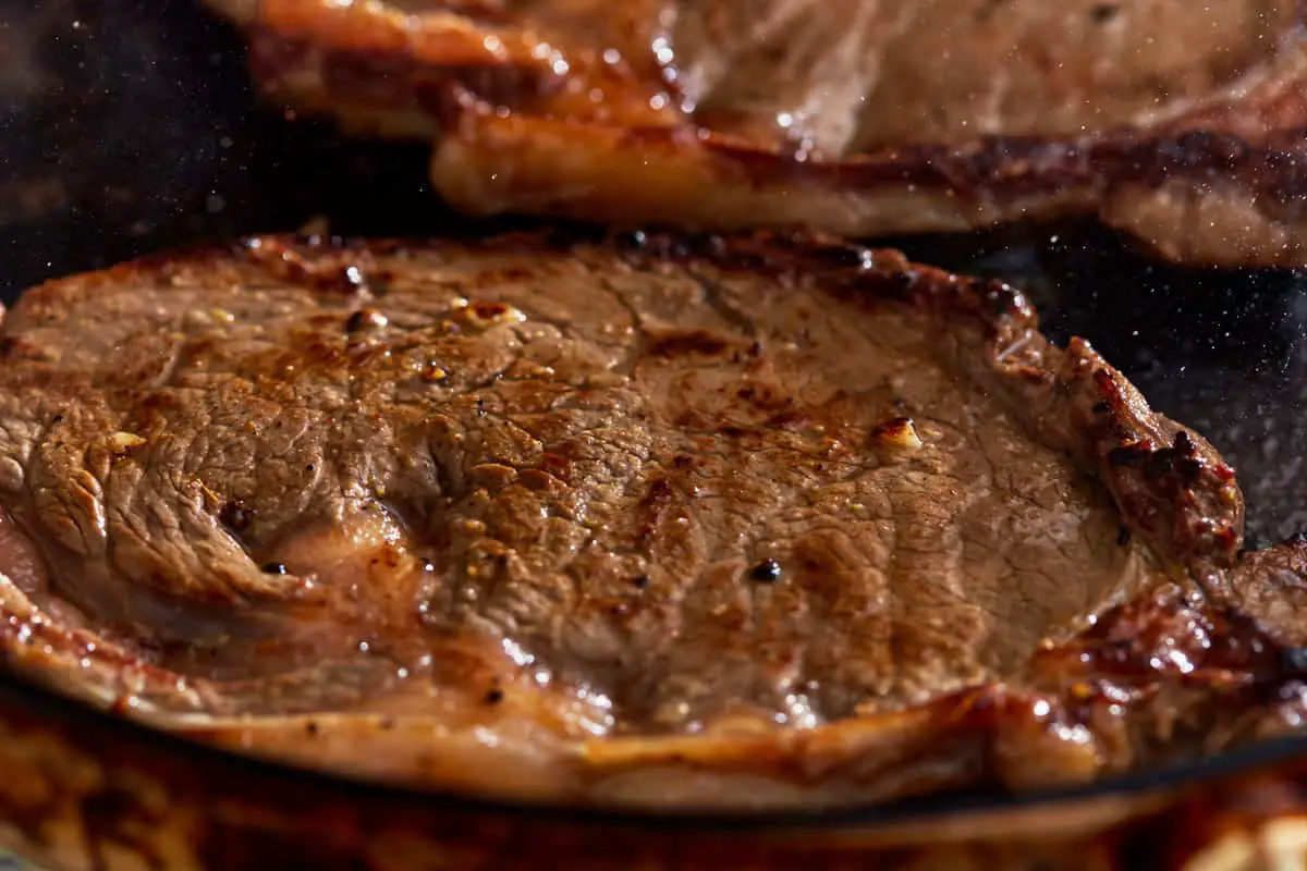 In einer Bratpfanne werden zwei Steaks gebraten.