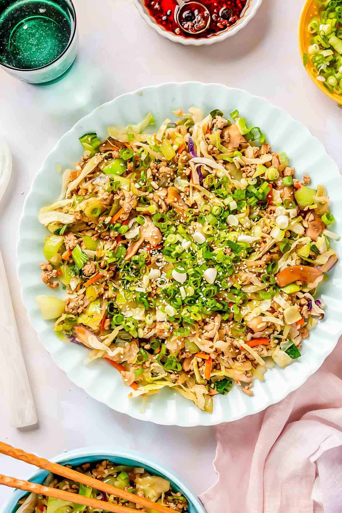 eggroll filling on a scalloped blue plate with fresh scallions and white sesame seeds sprinkled on top