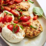 A plate of tomato basil chicken with balls of burrata.