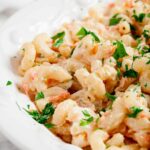 Close-up of a white dish filled with creamy Hawaiian macaroni salad garnished with chopped parsley.