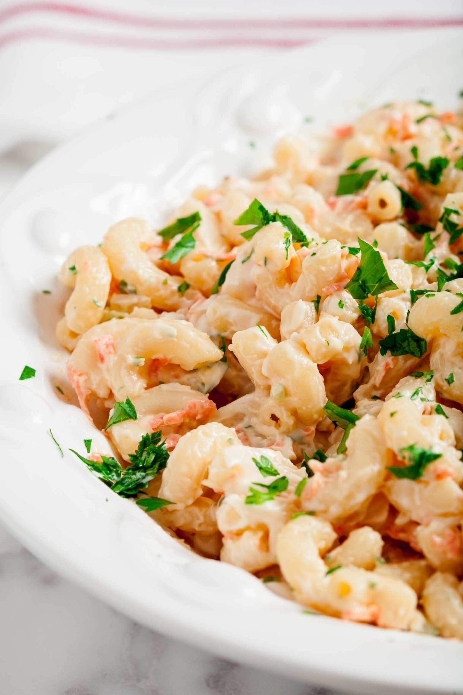 Close-up of a white dish filled with creamy Hawaiian macaroni salad garnished with chopped parsley.