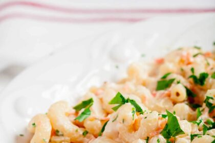 Close-up of a white dish filled with creamy Hawaiian macaroni salad garnished with chopped parsley.