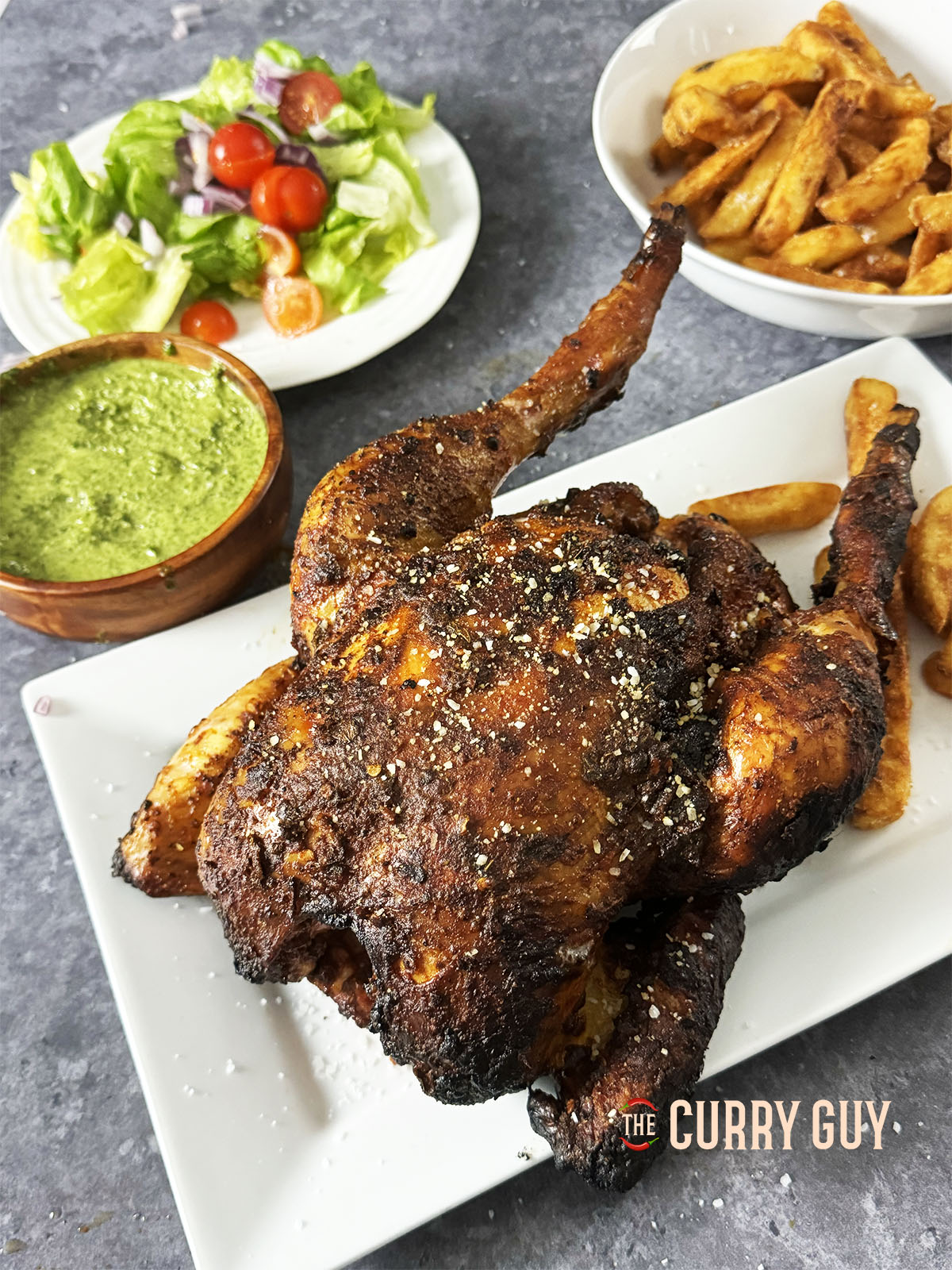 Puruvian Chicken – Pollo a la brasa, mit Beilagen auf einer Servierplatte am Tisch serviert.