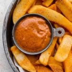 Overhead shot of seasoned french fries with a small bowl of red robin campfire sauce.