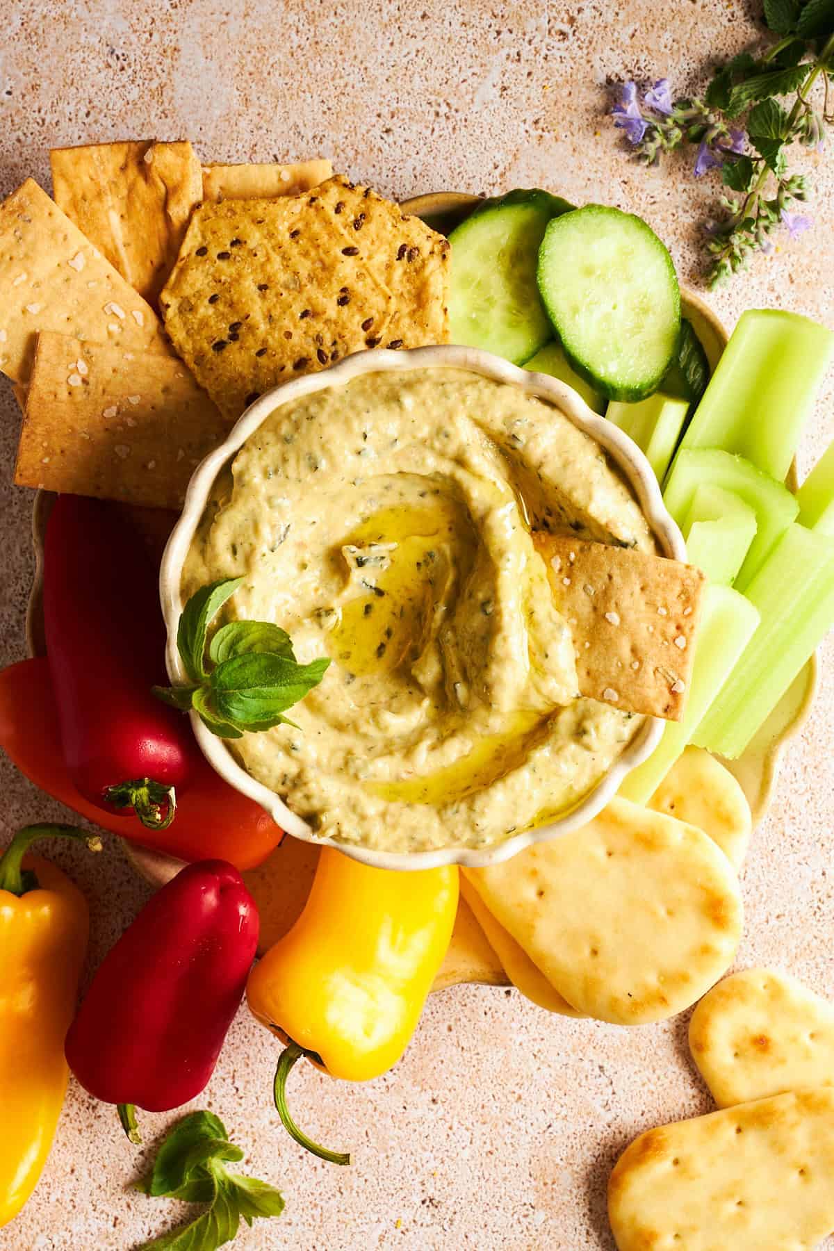 Eine Schüssel Zucchini-Dip auf einer Platte mit Gurken, Sellerie, Pita-Brot, kleinen Paprikaschoten und Crackern. 