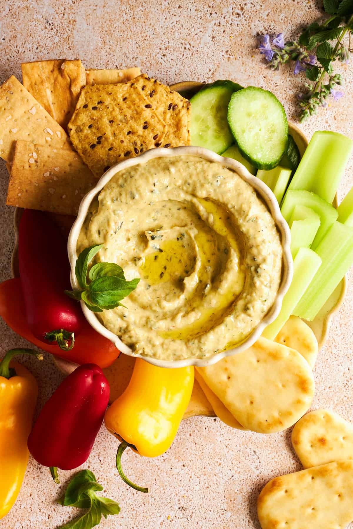 Eine Schüssel Zucchini-Dip auf einer Platte mit Gurke, Sellerie, Pita-Brot, Mini-Paprika und Crackern. 