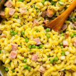 ham and pea pasta in a pot with a wooden spoon.