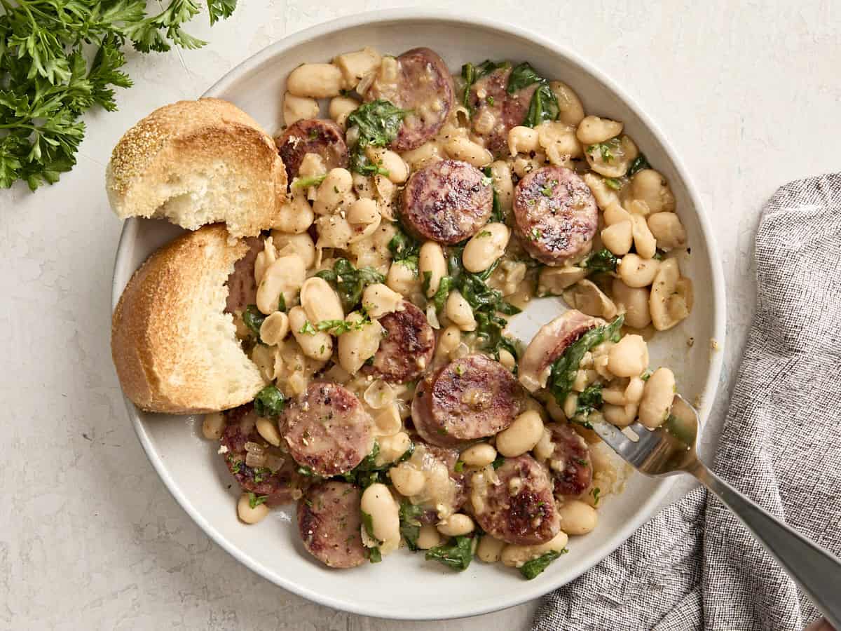 Draufsicht auf Hühnerwurst und weiße Bohnen auf einer Servierplatte mit geröstetem Brot an der Seite.