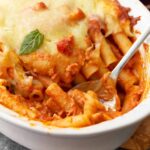 close up of baked ziti in a baking dish with a spoon.