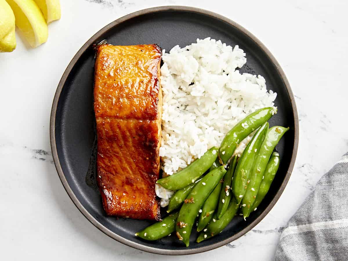 Draufsicht auf eine Portion Lachs aus der Heißluftfritteuse auf einem schwarzen Teller mit Reis und Erbsen.