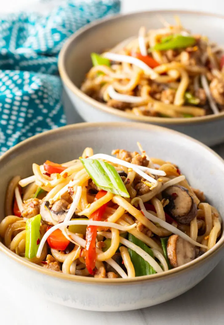 Schüssel mit Chicken Yaki Udon, garniert mit grünen Frühlingszwiebelscheiben und Mungobohnen.