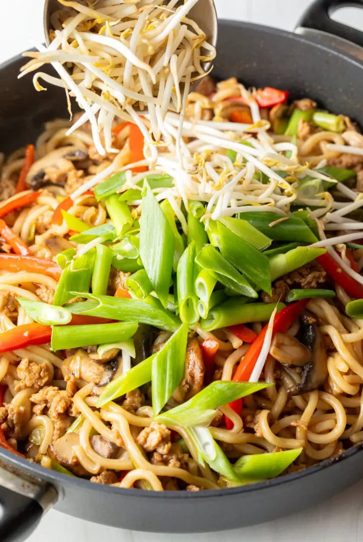 Nahaufnahme einer Pfanne mit Yaki-Udon-Nudeln, Sojasprossen und in Scheiben geschnittenen grünen Frühlingszwiebeln