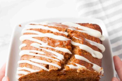 A plate with sliced zucchini carrot bread drizzled with cream cheese frosting, being held by two hands.