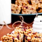 A close-up of three peanut butter cheerios bars with visible Cheerios and dried fruit, placed on parchment paper.