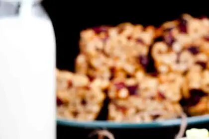 A close-up of three peanut butter cheerios bars with visible Cheerios and dried fruit, placed on parchment paper.